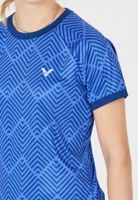 Blå atletisk T-shirt med et geometrisk mønster i forskellige nuancer af blå. Korte ærmer og rund halsudskæring med et lille logo.