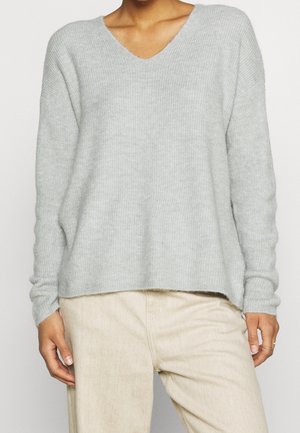 Maglione grigio chiaro a scollo a V con texture a coste, vestibilità rilassata e spalle cadenti, abbinato a pantaloni beige chiaro.
