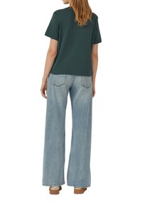 T-shirt en coton vert forêt à manches courtes, associé à un jean bleu clair à jambes larges, présentant un délavage et des poches arrière classiques.