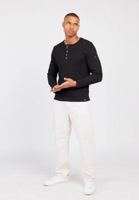 Top negro de manga larga con textura acanalada, cuello redondo y tapeta de tres botones, combinado con pantalones claros y zapatillas blancas.
