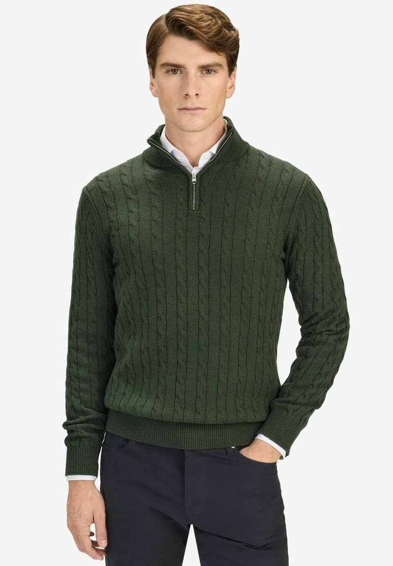 Donkergroen gebreid trui met een halve ritssluiting en een kabelbreipatroon, voorzien van ribgebreide manchetten en zoom. G gedragen over een wit shirt.