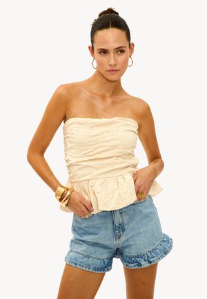 Haut sans bretelles crème avec un motif floral texturé, ourlet peplum ; associé à un short en denim bleu clair avec des bords festonnés.