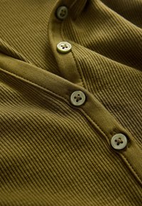 Olivengrønt ribstrikket stof med V-hals, der har fire runde knapper med fire-huls design og diskret syningsdetalje.