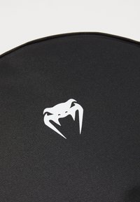 Superficie texturada negra con un logo blanco que recuerda a una criatura estilizada con garras, indicando un diseño duradero y funcional.