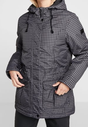 Person trägt eine grau-schwarz karierte Winterjacke mit Kapuze, Fronttaschen und Kordelzug, Hände nahe den Taschen.