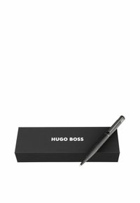 Stylo noir avec prise texturée et accents argentés, posé sur une boîte noire mate portant "Hugo Boss" en lettres blanches en gras.