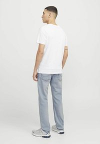 T-shirt blanche à manches courtes, jeans bleu clair et baskets grises. La tenue présente une coupe décontractée avec un minimalisme dans les détails.