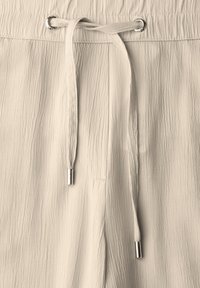 Beige, lightweight fabric pants with a textured surface, drawstring waist, and silver-tone accents on the drawstring tips.