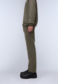 Olivgrön bomullströja och matchande byxor, i kombination med svarta slip-on skor. Tyget ser slätt ut; byxorna har en tapered stil.