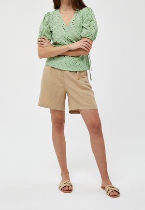 Haut en tissu éponge vert à manches courtes bouffantes, associé à un short en lin beige. Des sandales à glissière tan complètent la tenue.