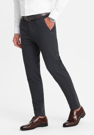 Pantalones tailored en gris oscuro con un corte ajustado y dos bolsillos laterales, combinados con zapatos marrones de cordones y un cinturón de cuero oscuro.