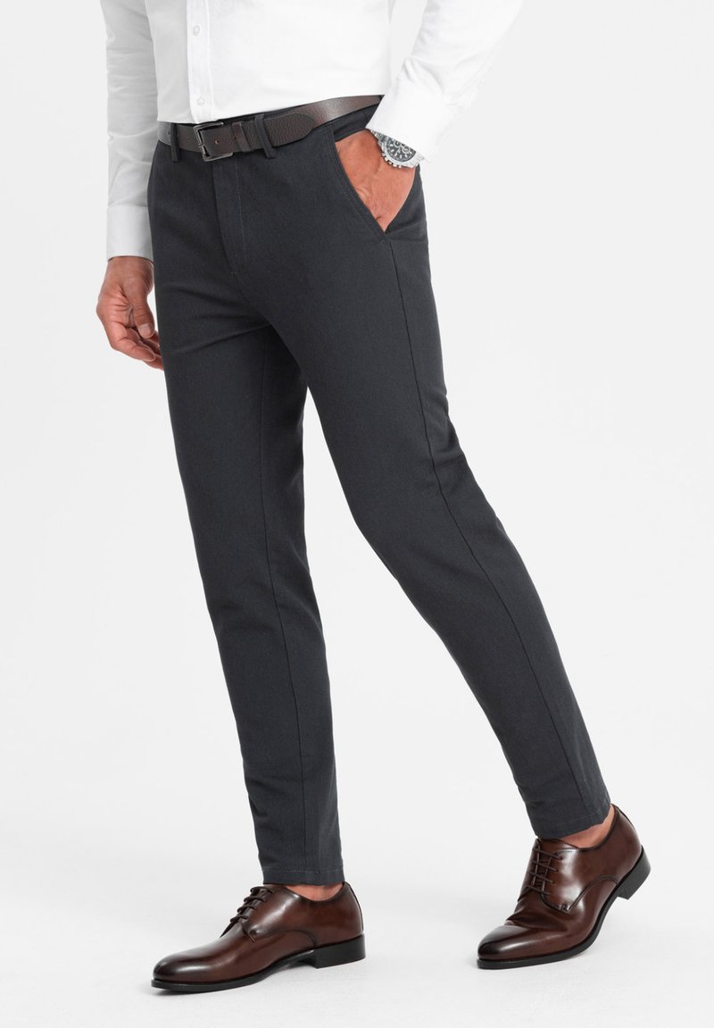 Dunkelgraue, maßgeschneiderte Hose im Slim-Fit-Stil mit zwei Seitentaschen, kombiniert mit braunen Schnürschuhen und einem dunklen Leder-Gürtel.