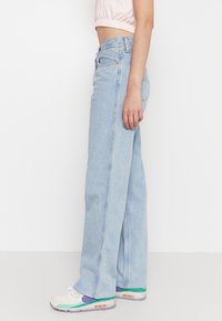 Jeans de tiro alto en azul claro, fabricados en denim, con un diseño de pierna recta y detalles de costura sutiles. Combinados con zapatillas coloridas.