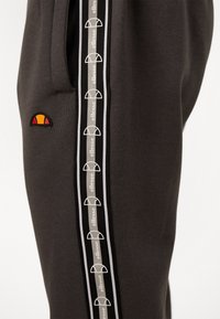 Charcoal gray sweatpants with a side stripe featuring repeated white ellesse logos and an embroidered ellesse logo patch near the pocket.