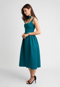 Tealowa midi sukienka z dopasowanym gorsetem, rozkloszowaną spódnicą i cienkimi ramiączkami. W komplecie z pasującym chokerem i czarnymi sandałami na obcasie.
