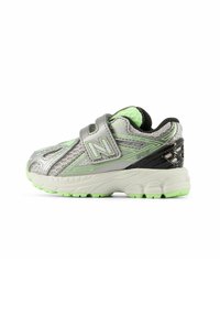 Silver athletic shoe with green accents and black details. Features a Velcro strap and textured mesh upper, designed for comfort and support.