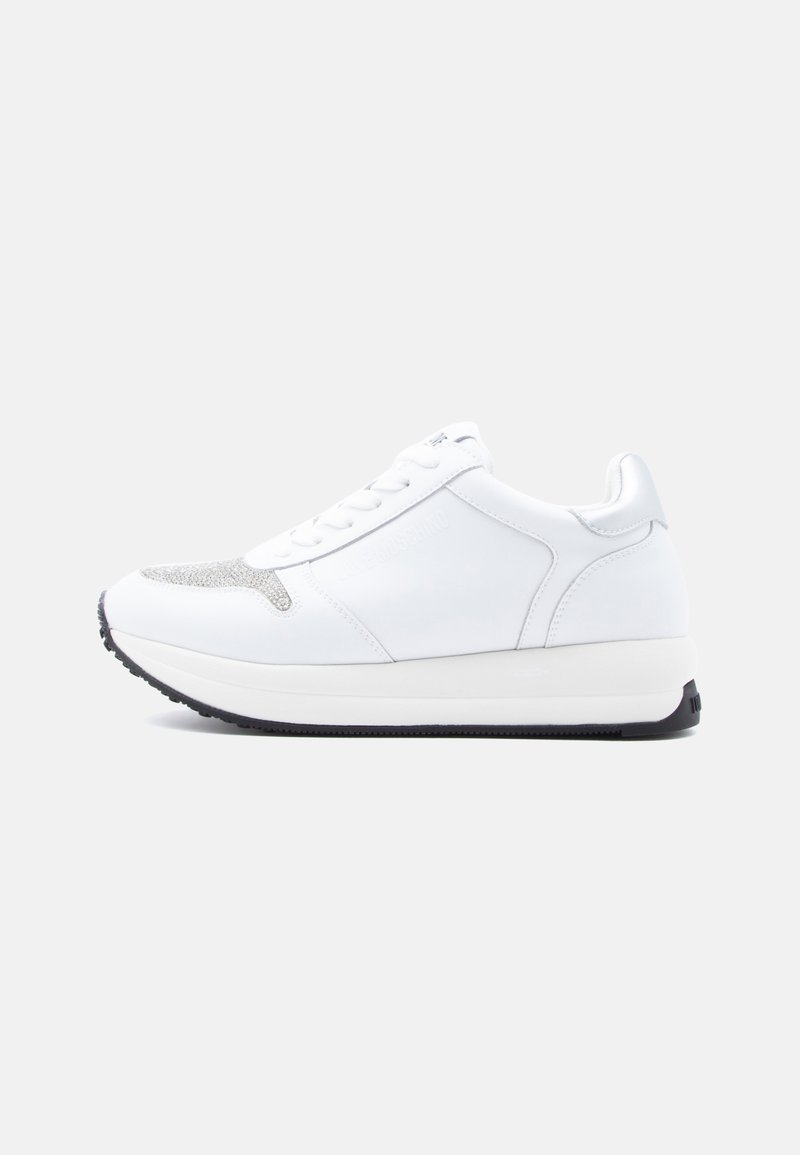 Λευκό αθλητικό παπούτσι με άνω μέρος από λείο δέρμα, υφασμένες ασημένιες λεπτομέρειες στη μύτη και λευκή σόλα με πλατφόρμα που διαθέτει μαύρη ελαστική εξωτερική σόλα.