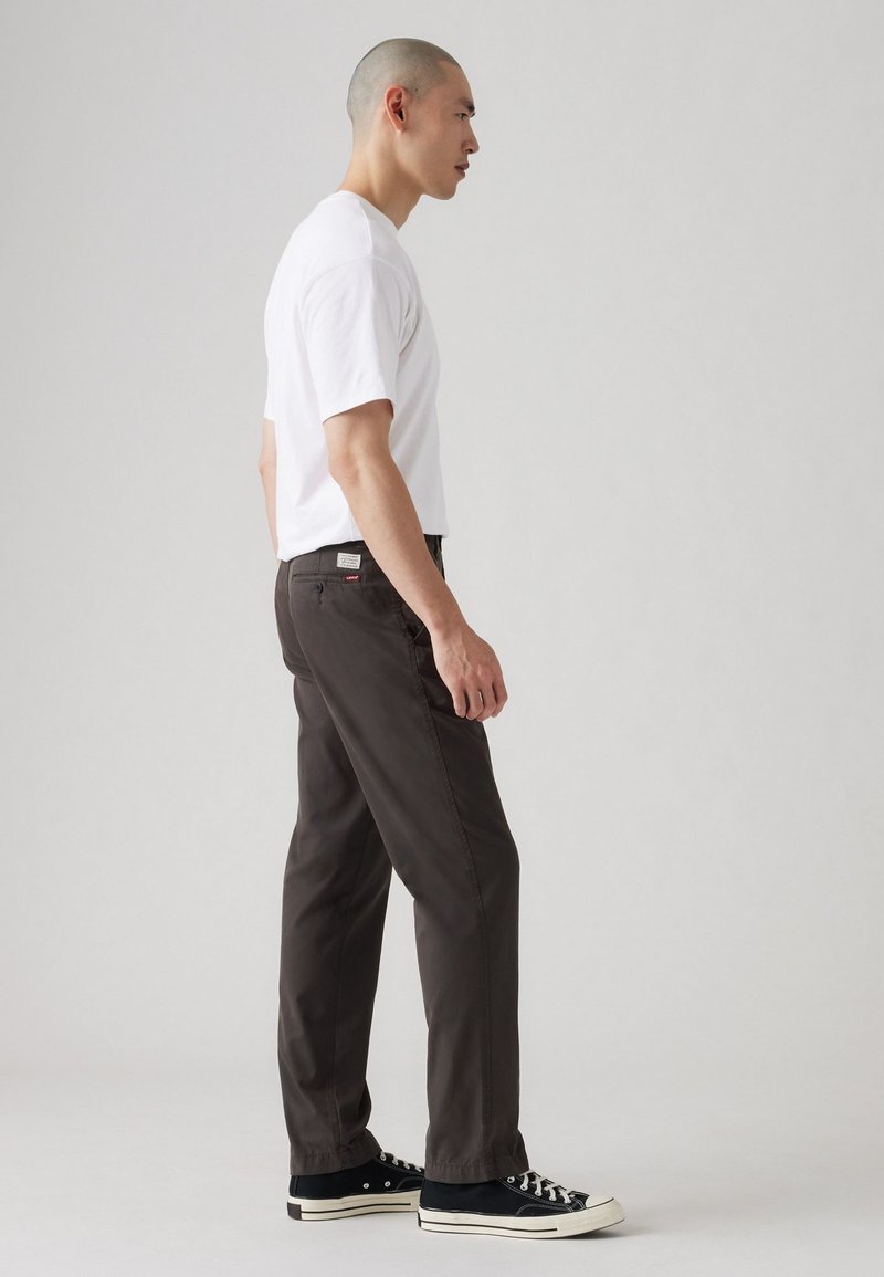 Pantalones gris oscuro hechos de una tela ligera, con un corte relajado, bolsillos clásicos y detalles de costura sutiles, combinados con una camiseta blanca básica.