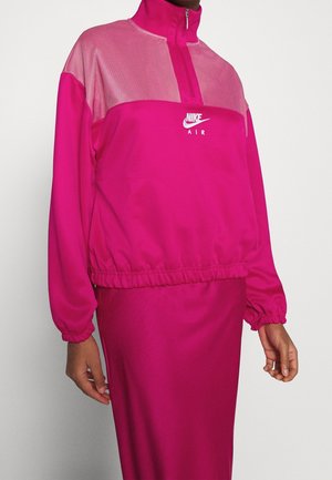 Person wearing a bright pink Nike Air pullover with mesh upper detail, quarter zip, elastic cuffs, and matching pink skirt.