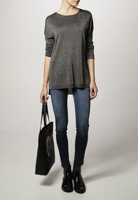 Haut à manches longues métallisé gris associé à un jean skinny noir et des bottines noires. Un sac tote noir avec un design circulaire est inclus.
