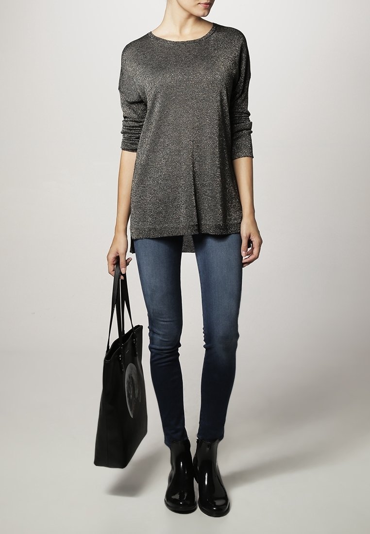 Haut à manches longues métallisé gris associé à un jean skinny noir et des bottines noires. Un sac tote noir avec un design circulaire est inclus.