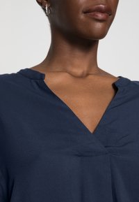 Top blu navy con scollatura a V, realizzato in tessuto morbido e con maniche corte. Un sottile dettaglio di cucitura sul collo ne migliora l'aspetto.