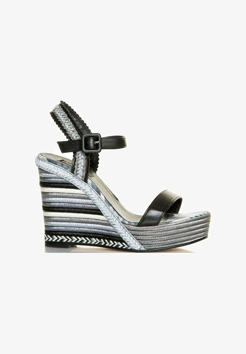 Sandalia cuña negra con una amplia tira en la puntera y tira ajustable en el tobillo. La cuña a rayas presenta texturas y patrones en gris, negro y blanco.