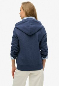 Sudadera con capucha en azul marino, fabricada en tejido texturizado, con puños y dobladillo acanalados, que muestra los puños de una camisa de capa visible debajo. Vista posterior completa.