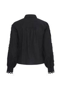 Blouse noire à manches longues vue de dos, avec une bordure en dentelle ajourée aux poignets et le long des manches, coupe ample et froncée.