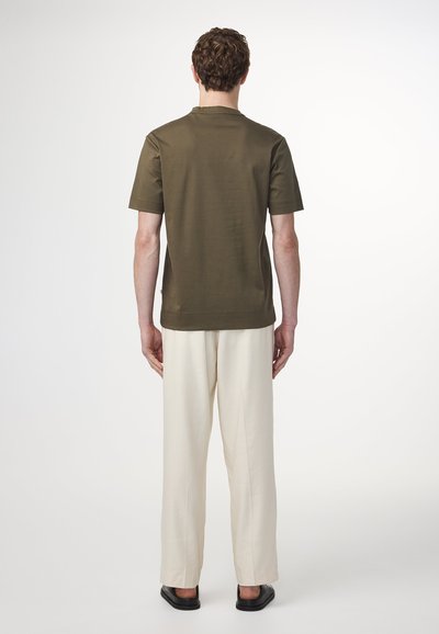 Olijfgroen T-shirt met korte mouwen en een relaxte pasvorm, gecombineerd met crèmekleurige wijde broek en zwarte platte sandalen. Gladde stof, minimalistisch ontwerp.