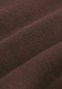 Brązowy materiał z teksturowanym splotem, lekko pognieciona powierzchnia i intensywny, głęboki kolor. Tkanina wydaje się miękka i trwała.