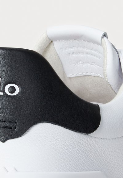 Artimas baltos sportinės batelės kulno vaizdas su juodu odiniu akcentu ir daliniu prekės ženklo "Polo" logotipu ant nugarinės etiketės.