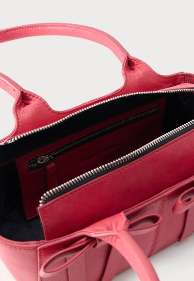 Κόκκινη δερμάτινη τσάντα χειρός με διπλές λαβές, επάνω φερμουάρ ανοιχτού τύπου και εσωτερική τσεπούλα με φερμουάρ, με την ετικέτα "Stand Studio".