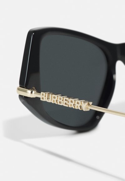 Mustat suorakulmaiset aurinkolasit tummilla linsseillä. Varressa on kultasävyinen metallinen osa, jonka koristaa kaiverrettu "BURBERRY"-logo.