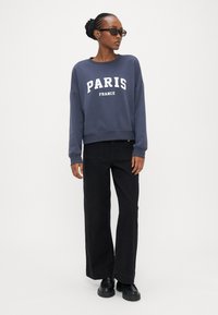 Felpa navy con scollo a girocollo e stampa "PARIS FRANCE", abbinata a pantaloni neri a gamba larga e scarpe platform nere. Tessuto dalla texture liscia.