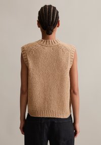 Beige sleeveless knitted sweater with a ribbed collar and hem. Chunky texture with visible stitches, shown from the back.