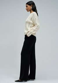 Crème geribbelde trui met lange mouwen, gecombineerd met zwarte wijde broek en zwarte puntige hakken. Eenvoudige en gestructureerde designelementen.