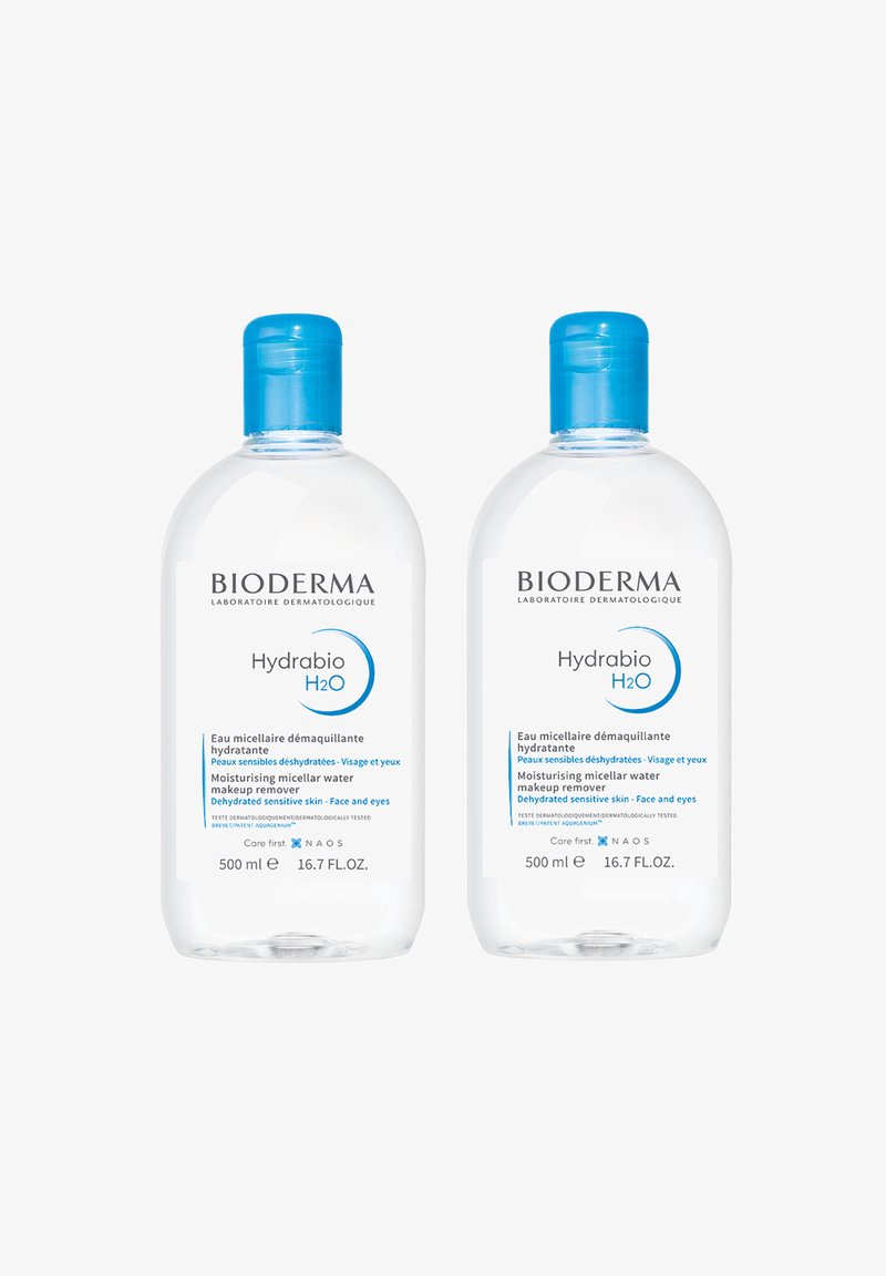 Bioderma Hydrabio H2O, due bottiglie trasparenti da 500 ml con tappi blu. Le etichette mostrano uno sfondo bianco e testi blu che descrivono gli utilizzi del prodotto.