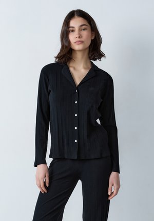 Das schwarze, gerippte Schlafanzugset besteht aus einem langärmeligen, knöpfbaren Hemd mit einer Tasche und passenden Hosen. Weicher Stoff und elegante Linien. Weiße Knöpfe.