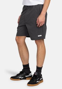 Graue Shorts aus leichtem Material mit einem elastischen Bund. Bemerkenswerte Details sind ein kleines Markenschild am Saum und eine lässige Passform.