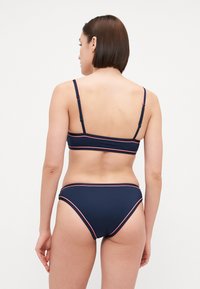 Tums zilbs bikinis ar bandeau topu un atbilstošām apakšdaļām ar kontrastējošām sarkaniem akcentiem, izgatavots no gludas, elastīgas auduma.