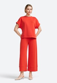 Rode cropped sweatshirt en wijde broek van zachte stof met een ontspannen pasvorm. Witte slingback schoenen maken de look compleet.