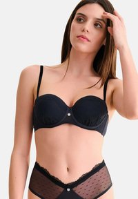 Ensemble soutien-gorge et culotte noir avec des accents en dentelle et un motif à pois. Le soutien-gorge dispose d'un soutien armé et de bretelles réglables.