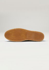 Suela de goma con un patrón texturizado en color marrón claro, que presenta formas geométricas elevadas y un borde suave.