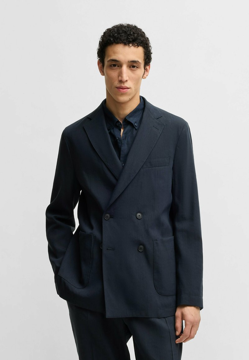 Dobbeltbrystet mørkeblå blazer lavet af glat stof med to sidelommer, notch-lapel og en brystlomme. Skræddersyet pasform.