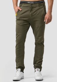 Maslinaste cargo hlače slim fit kroja, s žutim detaljem na džepu, šivenim detaljima i crnim pojasom s "INDICODE" brendom.