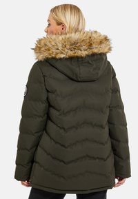 Donzen jas in donker olijfgroen met een capuchon en faux fur rand. Met een gequiltde textuur en een ronde patch op de linker schouder.