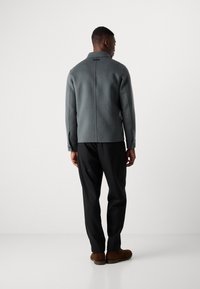 Grey wool blend jacket with a collar, back seam detailing, and buttoned cuffs, paired with black trousers and brown shoes.