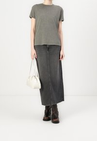 Oliwkowa koszulka z krótkim rękawem połączona z długą szaro-denimową spódnicą. Modelka trzyma małą białą torebkę i nosi brązowe botki za kostkę z klamrami.