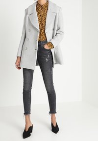 Harmaa kaksirivinen takki leopardikuvioisen topin päällä, yhdessä mustien pillifarkkujen kanssa, joissa on repaleiset reunat, ja mustat korkokengät.